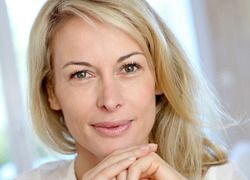 Smiling blond woman holding clasped hands under chin